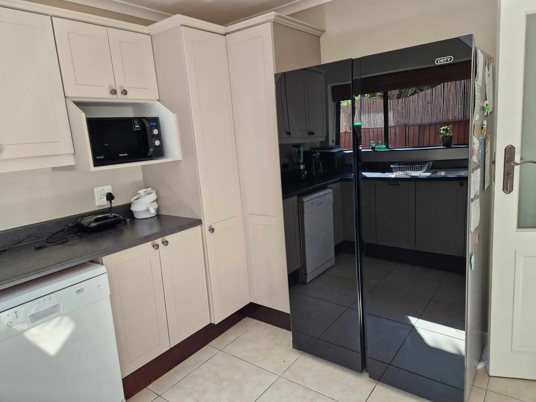 Scullery with a black fridge and white cabinets